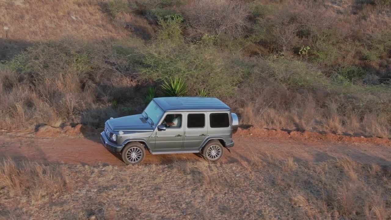Vista aerea con drone di un SUV fuoristrada che percorre una strada sterrata attraverso praterie secche e una campagna aspra durante l'ora d'oro a Oaxaca, Messico.