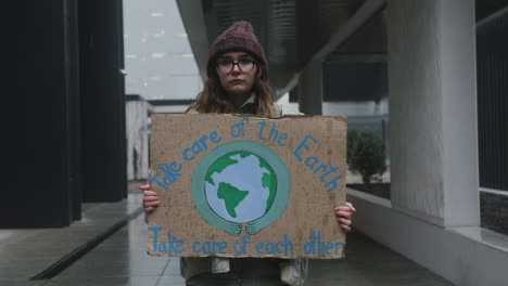 Retrato-De-Una-Joven-Activista-Con-Pancarta-Haciendo-Una-Protesta-Silenciosa-Contra-El-Cambio-Climático-Mientras-Mira-La-Cámara