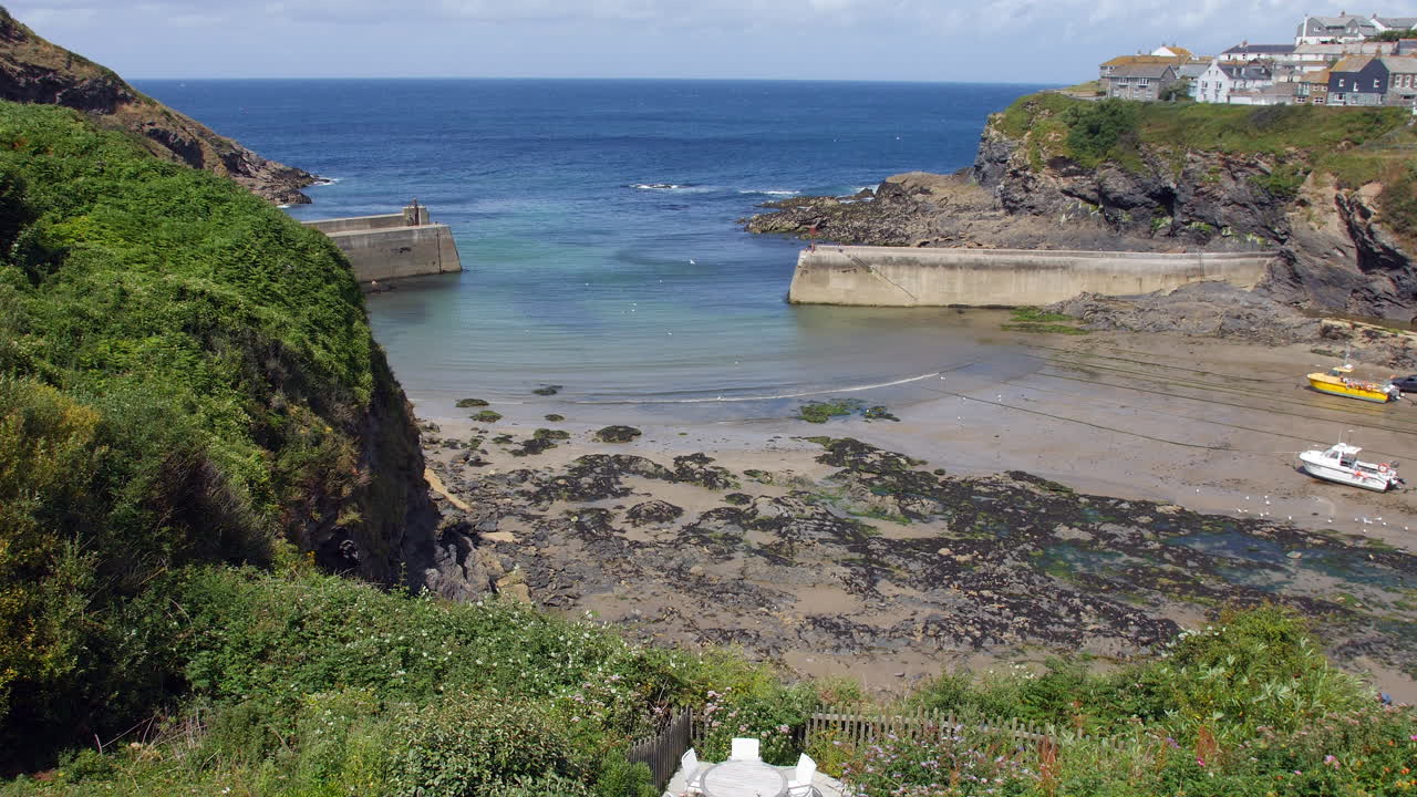 A harbor at low tide in Port Isaac Cornwall with boats grounded on sand and seaweed covered rocks framed by rugged cliffs and breakwaters marking the edge of Portwenn village