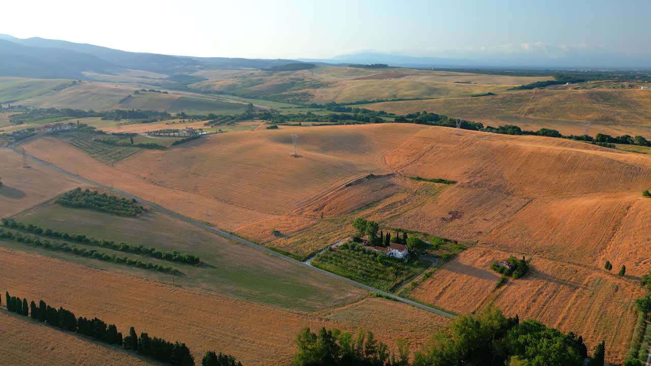 Warm golden sunlight illuminating rolling tuscan hills, revealing verdant farmland, scattered houses, and cypress trees creating serene mediterranean landscape