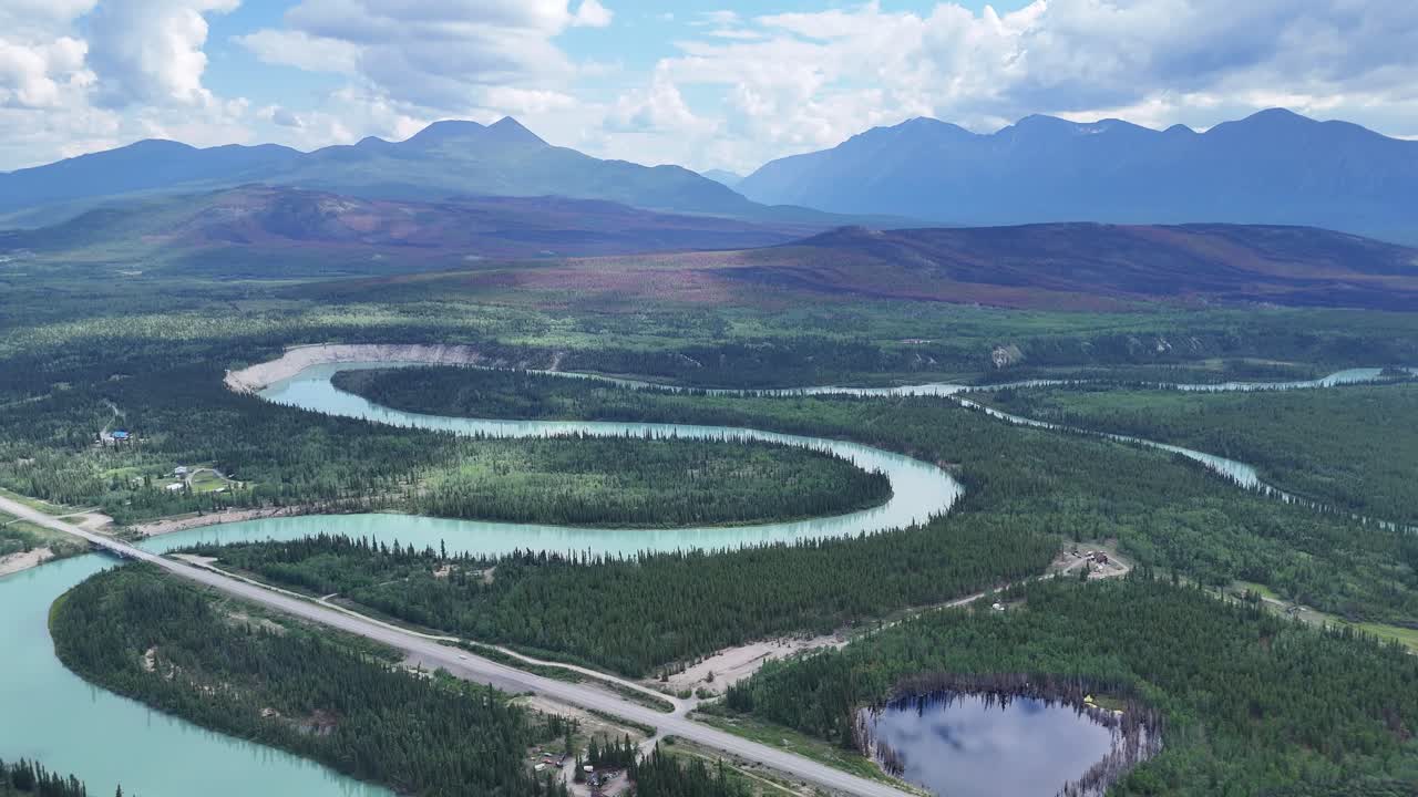 Majestic turquoise river carves through vast green forest towards distant blue mountains under a dramatic sky in Alaska