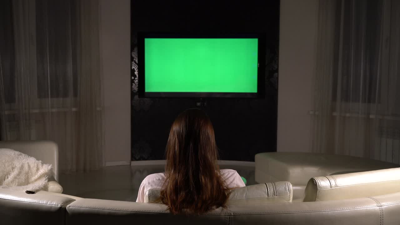 소녀는 어두운 방에서 녹색 화면으로 tv를 보고 있습니다.