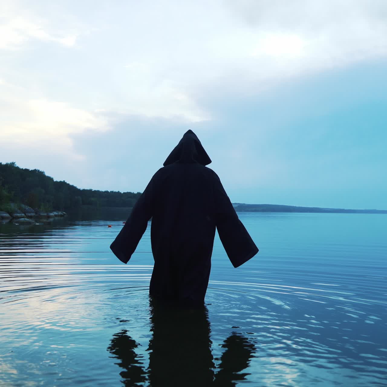 Scary figure in black mantle in the river. Halloween costume.