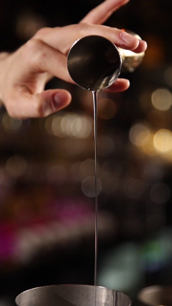 Barman che versa liquido dal jigger in uno shaker per cocktail al rallentatore