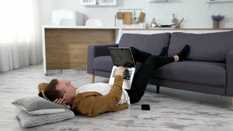 freelancer working at home. tired student studying on a laptop while laying on a floor with his legs on sofa. remote job.