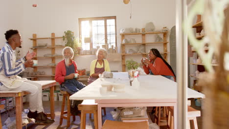 Happy-diverse-group-of-potters-drinking-coffee-and-discussing-in-pottery-studio