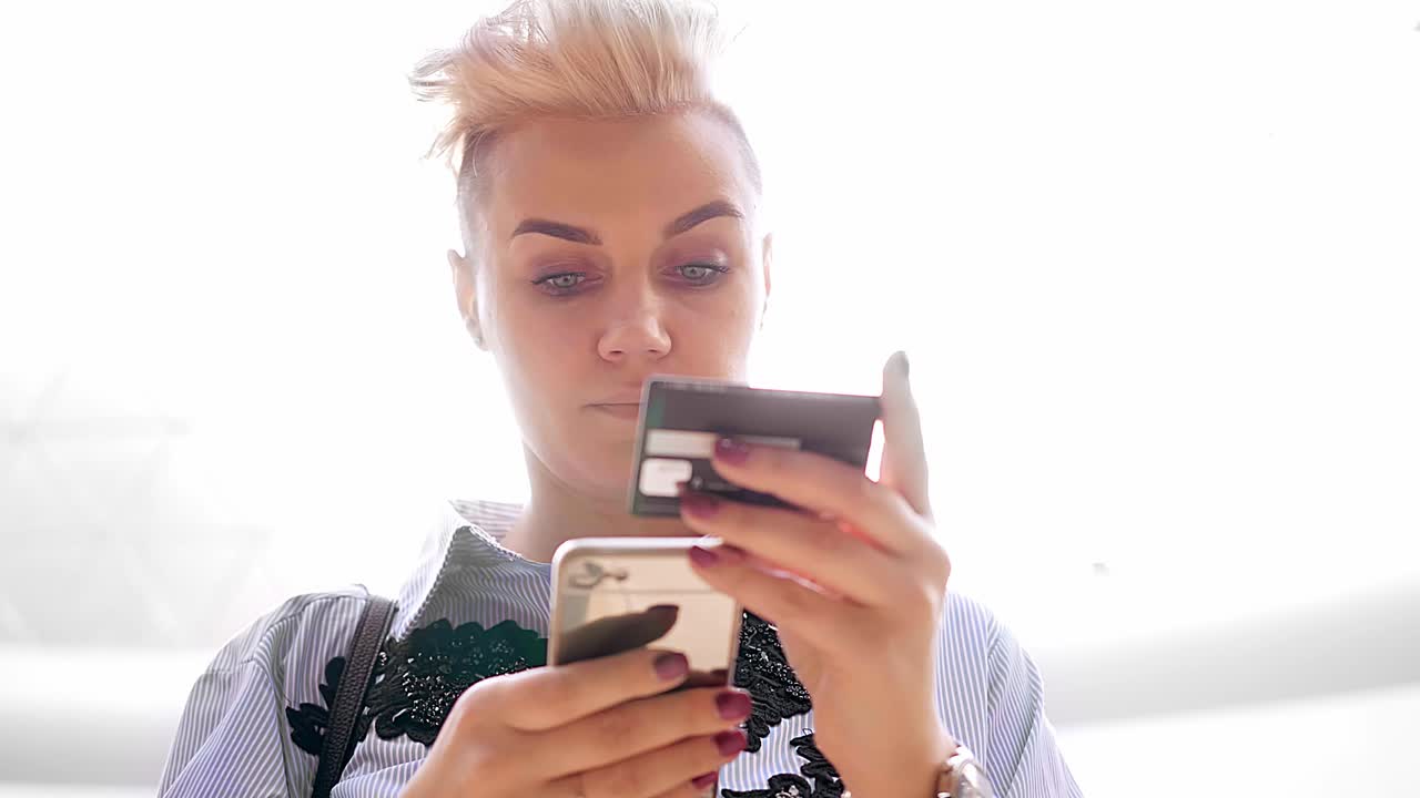 manos cerradas sosteniendo una tarjeta de crédito y usando un teléfono inteligente móvil en el interior, compras en línea, mujer feliz.