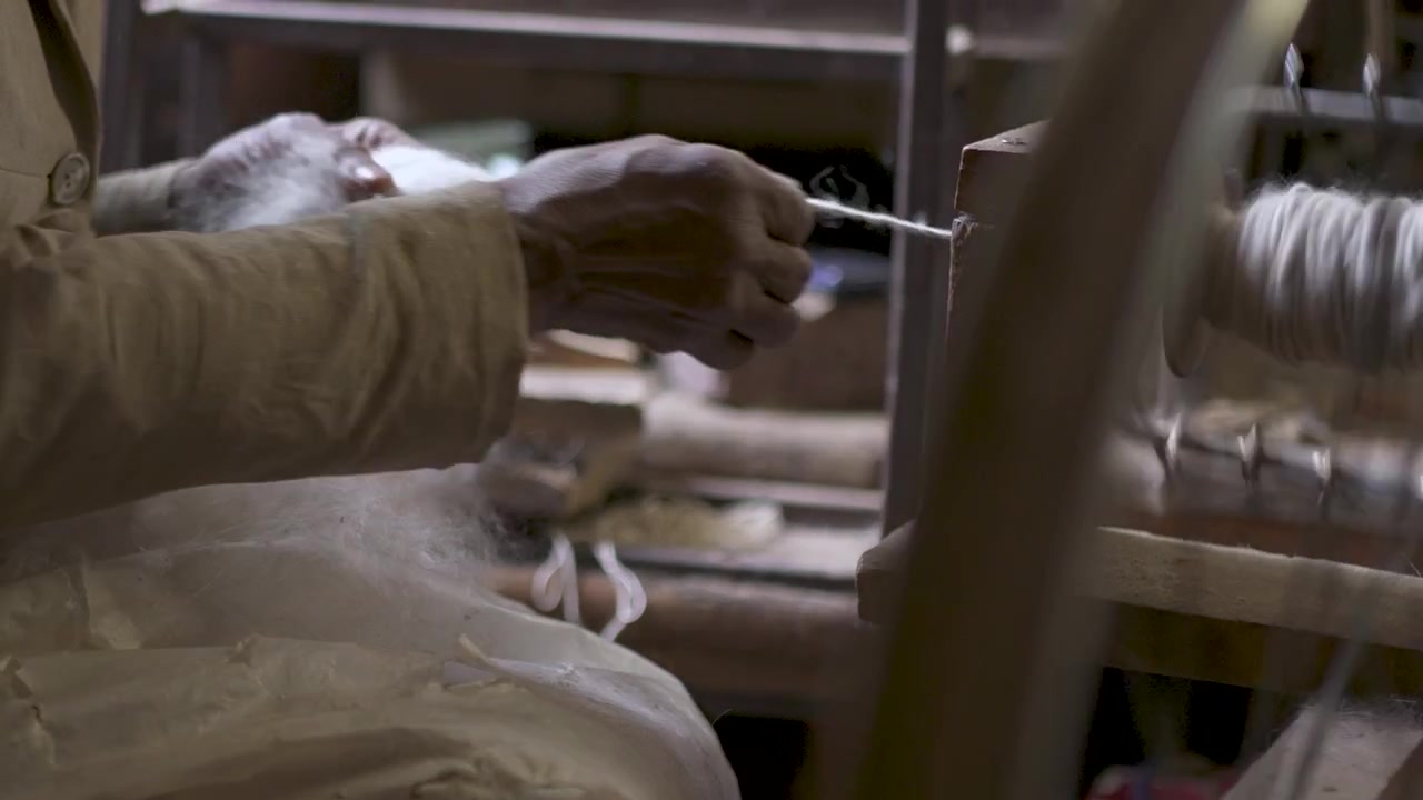 Skillful hands spin wool yarn on a makeshift wheel, highlighting the craft's intricate process. Suitable for cultural documentaries or educational content.