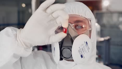 closeup portrait of scientist man in protective suit and respirator examining red pill