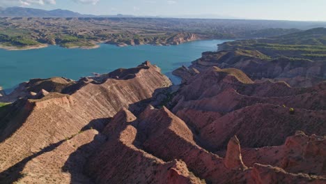 flight over reddish badlands and reservoir at sunset