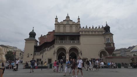 people walk across the vibrant main square in krakow, poland, with st. mary's basilica visible. the bustling atmosphere is highlighted by tourists and locals enjoying the historic architecture.