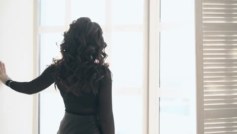 young-slim-long-haired-woman-approaches-bright-windows