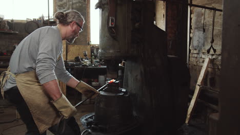 blacksmith forging iron rod with pneumatic hammer