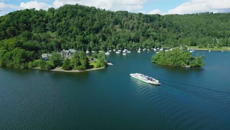 Erhöhte-Rotierende-Luftdrohnenansicht-Der-Autofähre-Auf-Dem-Lake-Windermere-Nähert-Sich-Sawrey-An-Einem-Sonnigen-Sommermorgen-Mit-Wellen-Auf-Den-Wasserwolken-Und-Weitreichendem-Blick-Auf-Die-Berge-Den-See-Hinunter