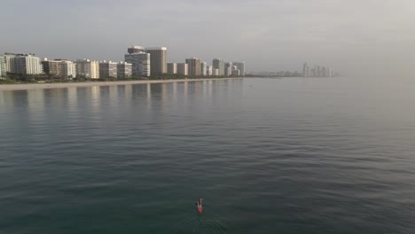 sunrise aerial: stand up paddleboarder on calm ocean at surfside beach