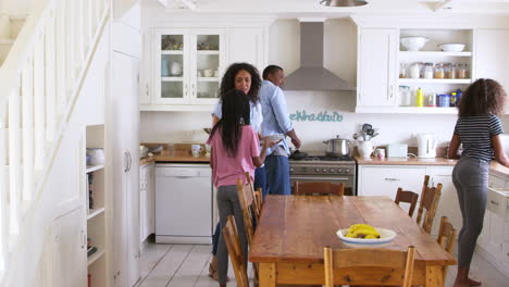 family with teenage children laying table for meal in kitchen