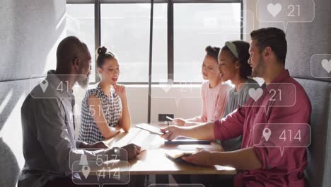 Anmation-of-social-media-icon-floating-over-team-of-diverse-colleagues-discussing-together-at-office