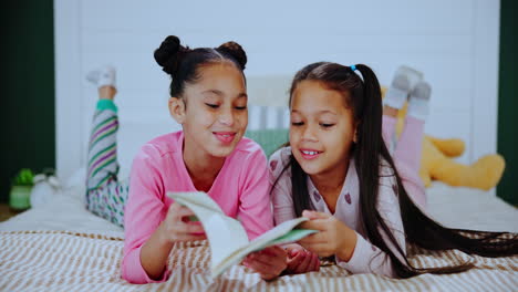 two young girls reading together in bed