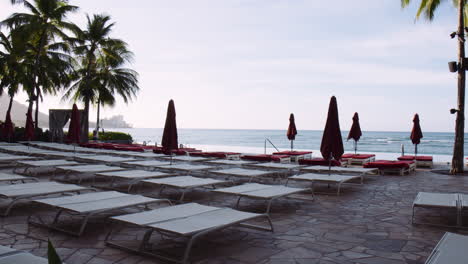 Tumbonas-De-Lujo-Con-Sombrillas-En-La-Terraza-De-Piedra-Junto-A-La-Piscina-Infinity,-Frente-A-La-Playa-De-Waikiki,-Hawaii,-Wide-Shot