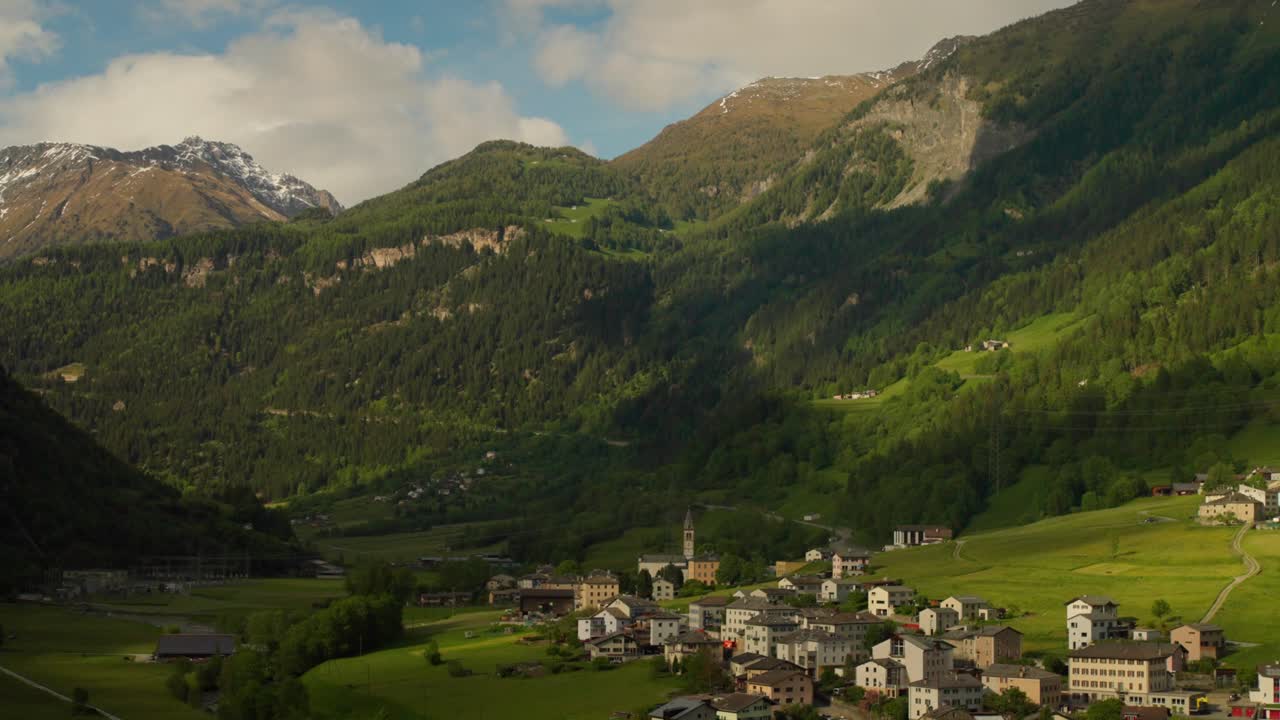 Ripresa grandangolare di una pittoresca cittadina di montagna circondata da lussureggianti pendii verdi e cime aspre nelle Alpi svizzere.
