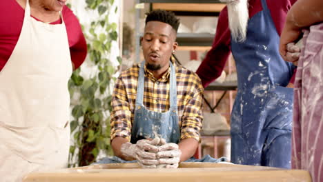 happy african american male potter and others, using potter's wheel in pottery studio, slow motion