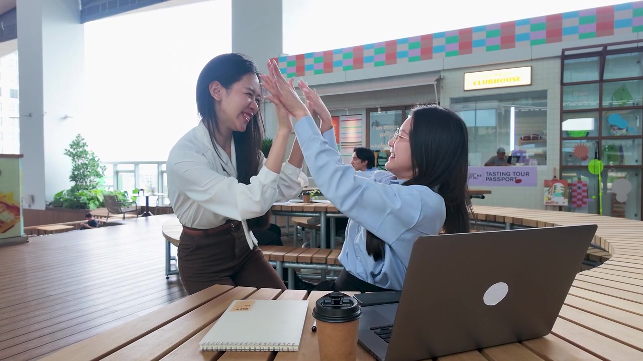 モダンなオフィスでハイタッチをして成功を祝う2人の若いアジア人女性