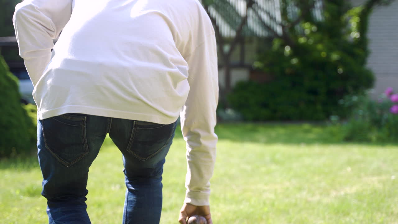 화창한 날 공원에서 페탕크 공을 던지는 백인 청년의 뒷모습