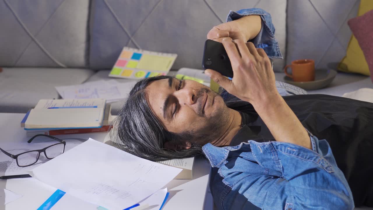 hombre de negocios perezoso sentado en casa mirando el teléfono y perdiendo el tiempo en el trabajo.