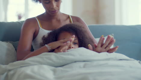 dolly shot of relaxed african american mum and daughter spending lazy weekend in bed, holding hands