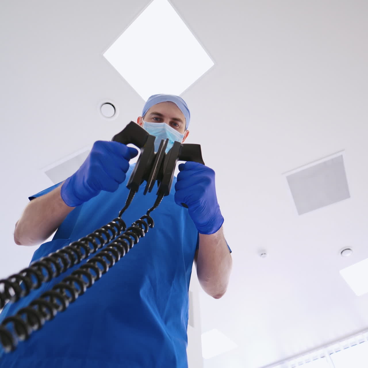 Doctor holds defibrillator. Male specialist in medical uniform use medical equipment for saving patient's life in clinic. Close-up.