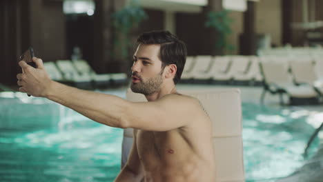 Nahaufnahme-Eines-Fröhlichen-Mannes,-Der-Am-Liegestuhl-Am-Pool-Ein-Selfie-Mit-Dem-Mobiltelefon-Macht.