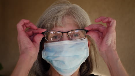 an aging woman wearing a medical patient mask in the hospital putting on her prescription eye glasses