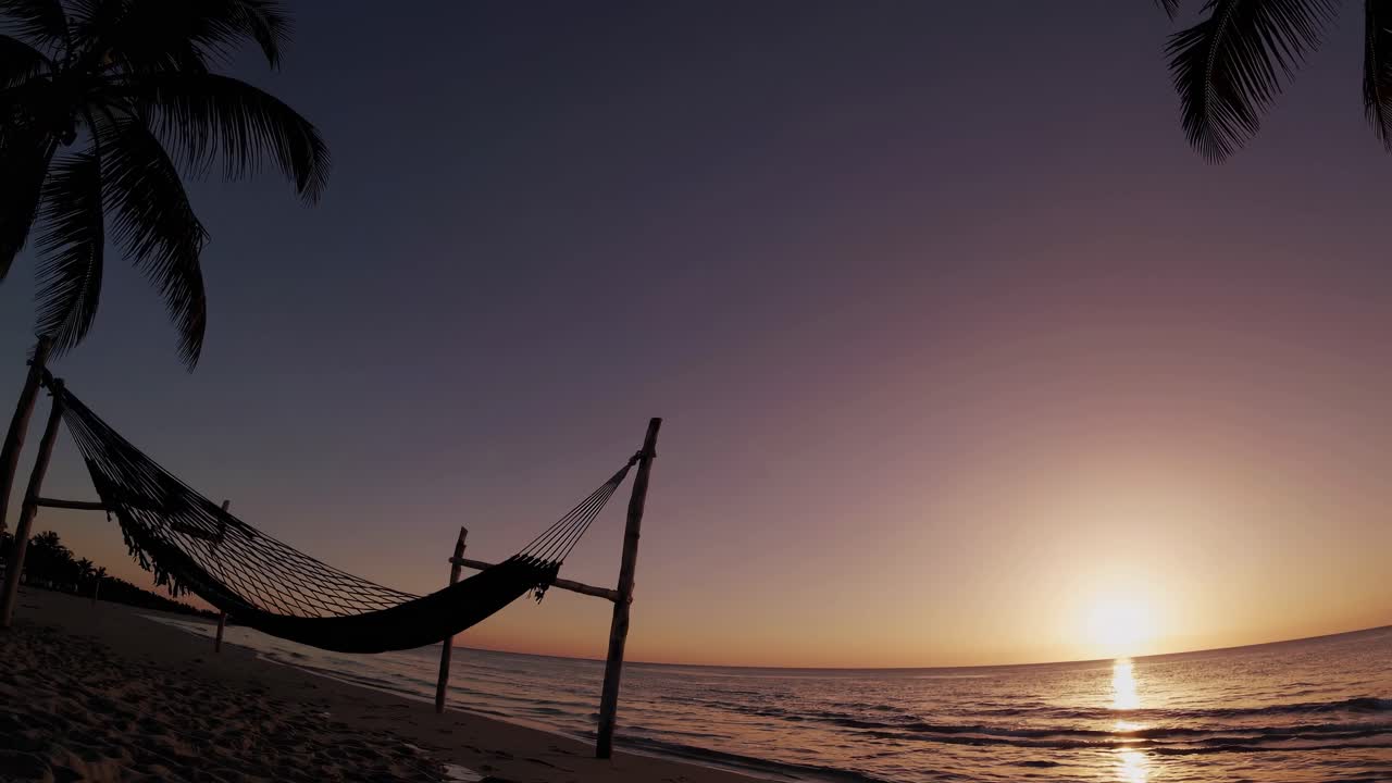 A serene beach sunset with a hammock, captured in a wide-angle shot