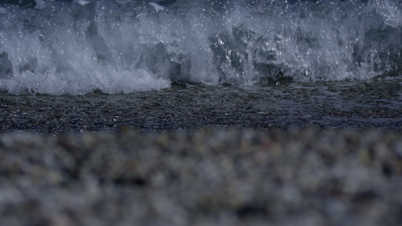 Small waves breaking on the shore of pebble beach in Marbella Spain, 4K, Slow Motion