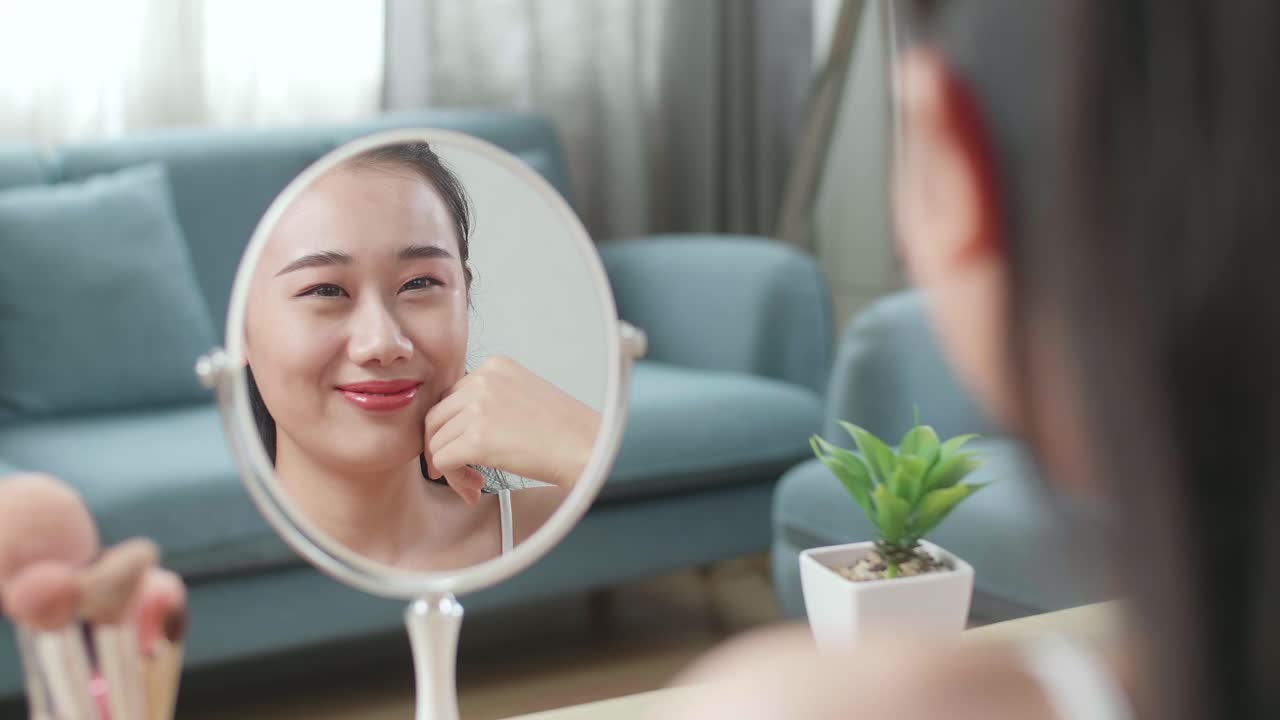 거울에서 반사 아름다운 젊은 아시아 여성은 그녀의 얼굴을 만지고 집에서 메이크업 적용 후 미소