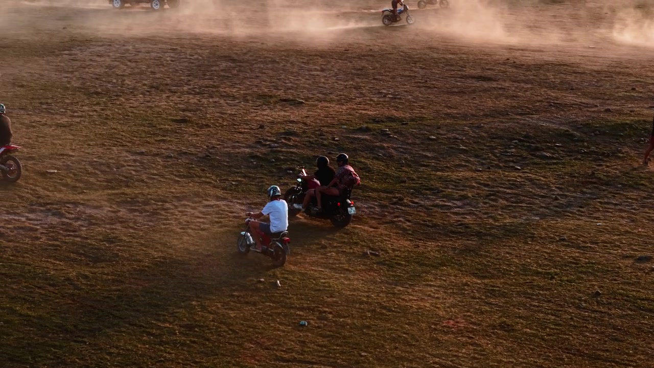 Motociclisti che attraversano un campo aperto polveroso al tramonto