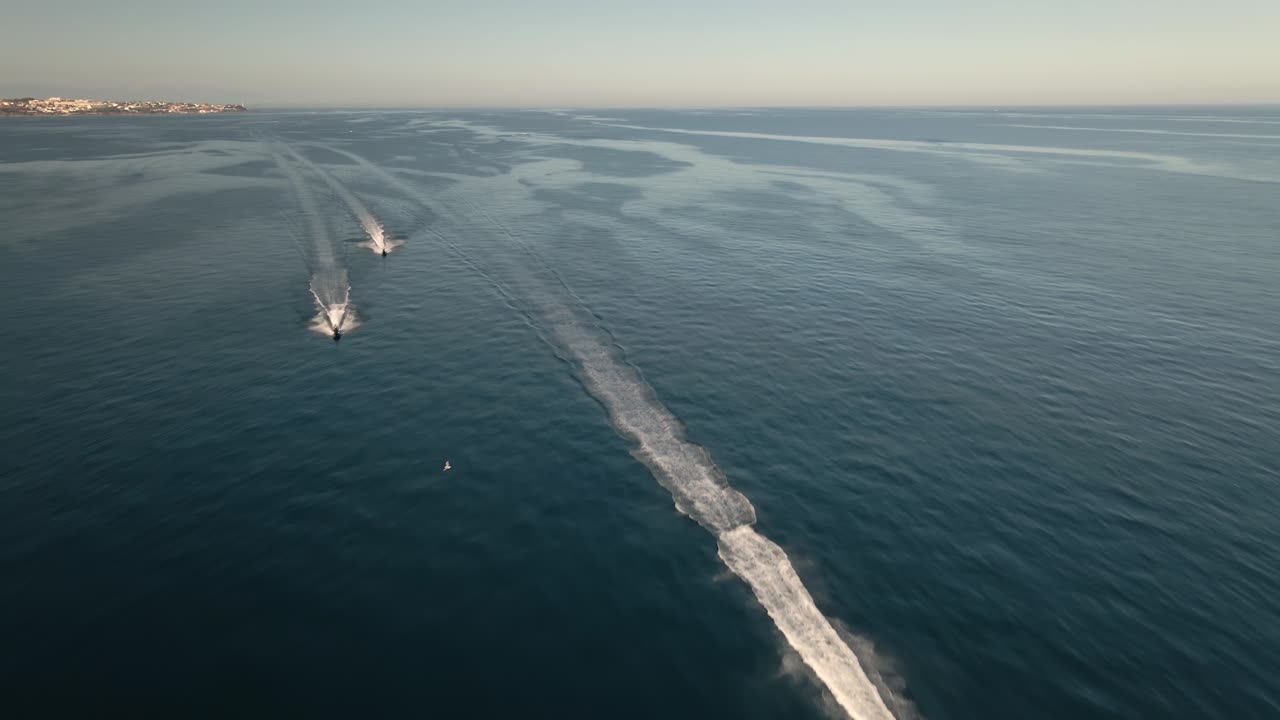 vista aérea por encima de la actividad de ocio de jet ski acelerando rápido a través de estelas oceánicas dejando estela inclinada hacia el horizonte