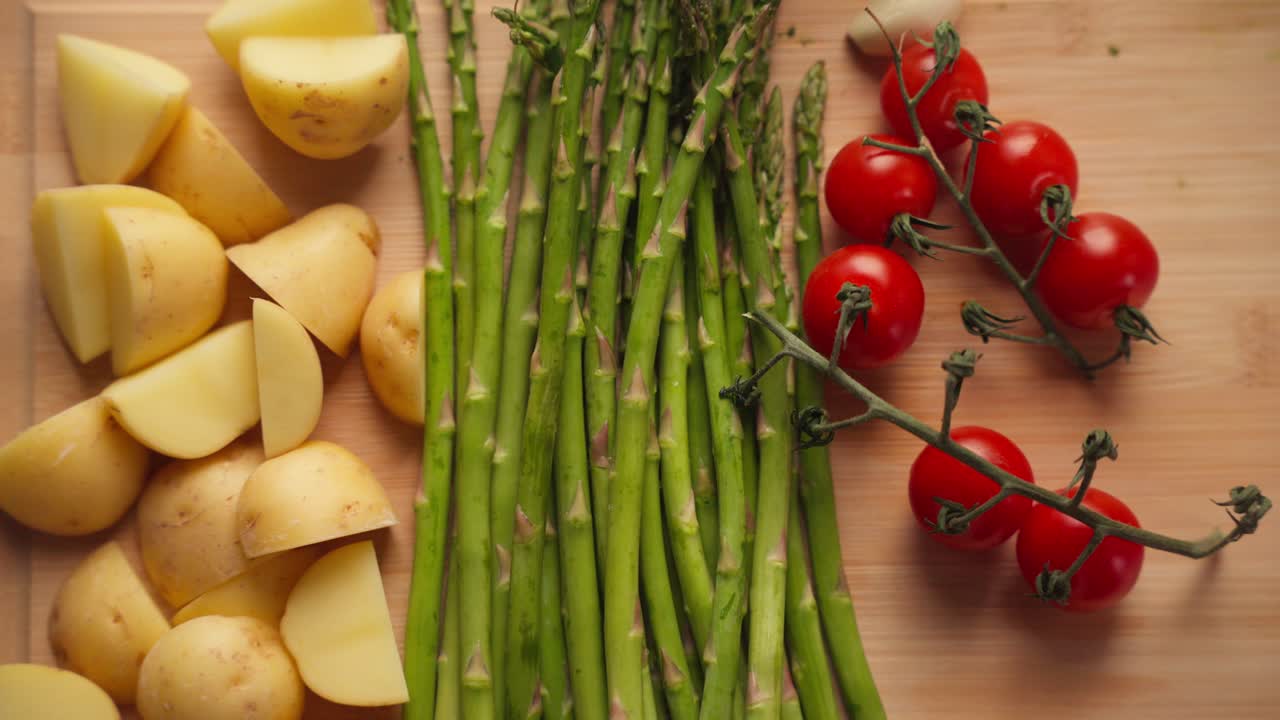Patate, asparagi, pomodori e cipolla sono disposti ordinatamente su un tagliere di legno, pronti per la preparazione in una cucina casalinga