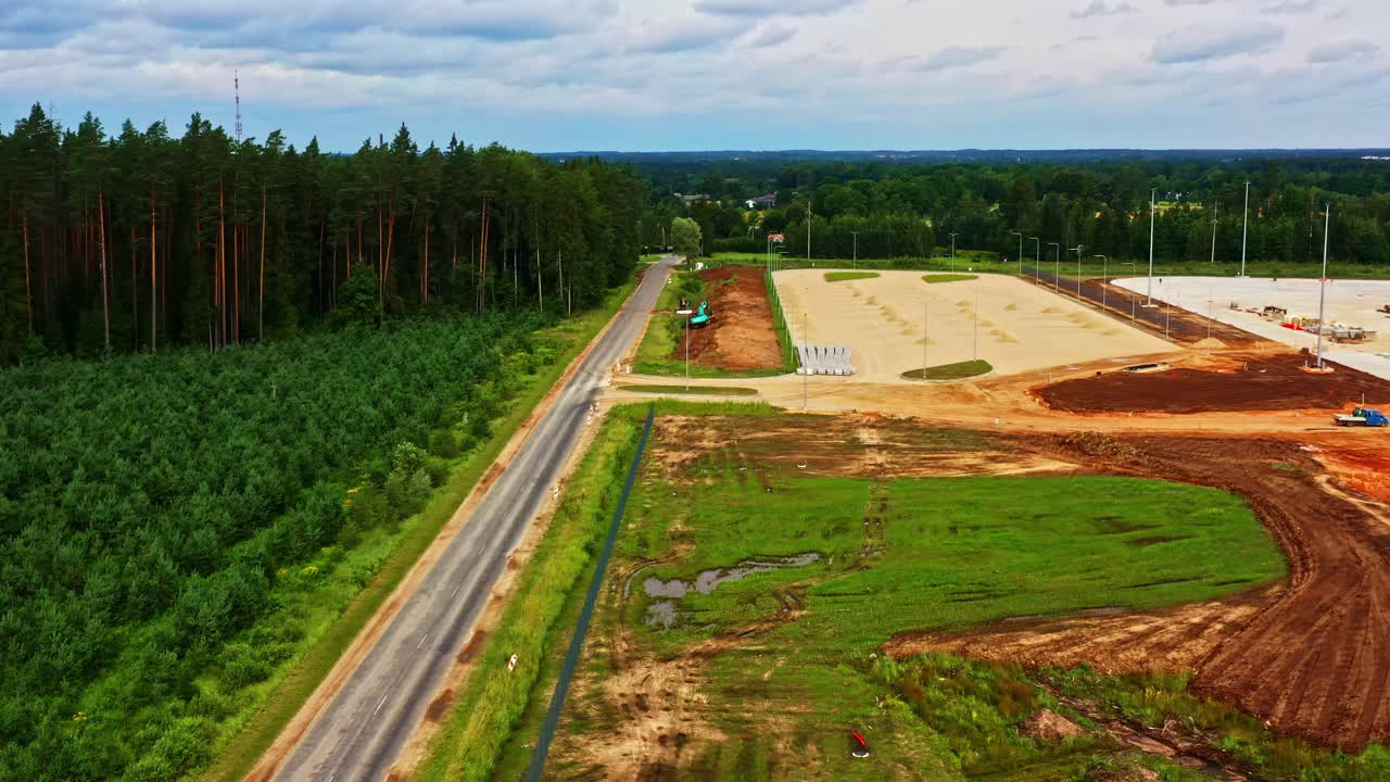 Excavator At Work At Construction Site In Rural Landscape With Forest In Background. wide drone shot