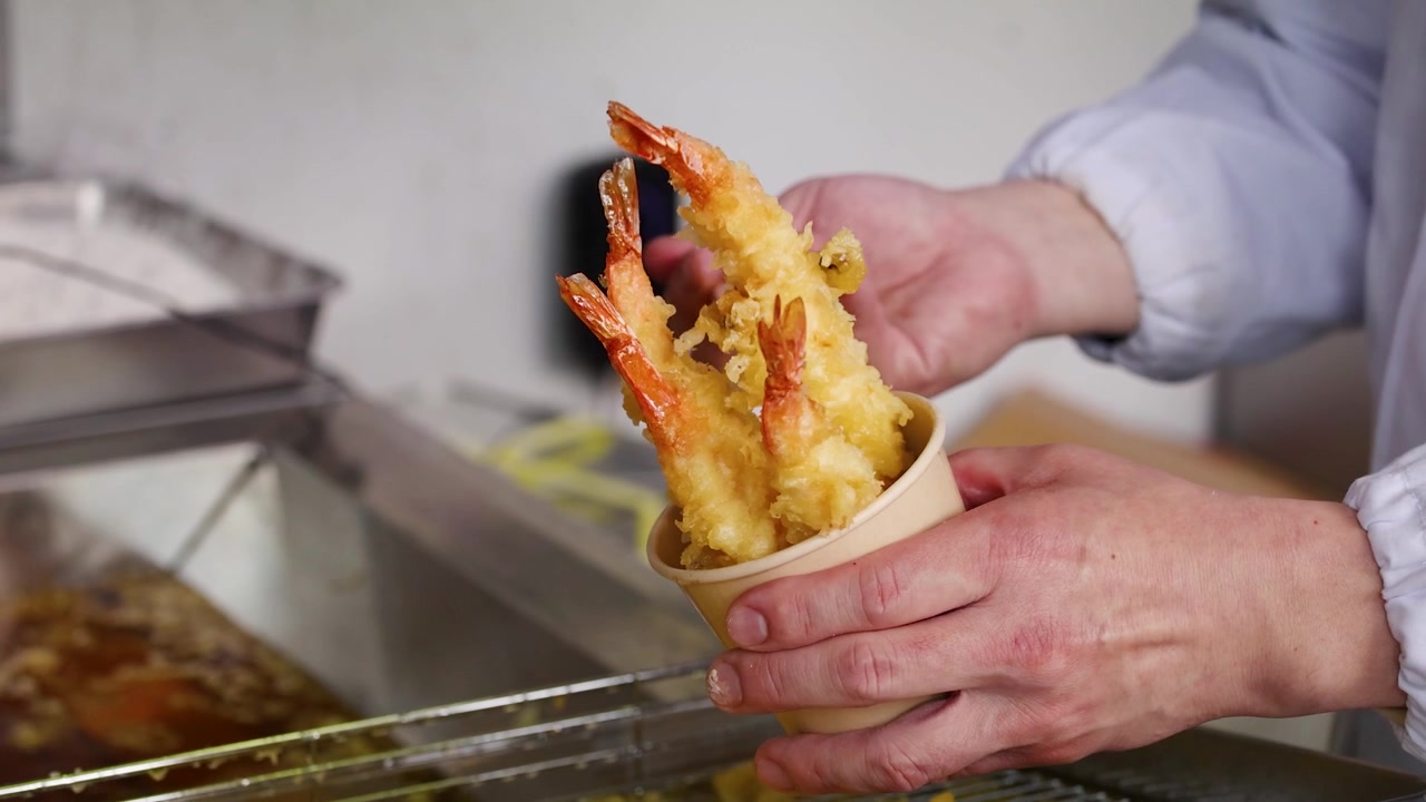Lo chef usa le bacchette per mettere i gamberi fritti in una coppetta di carta in una bancarella di Tokyo