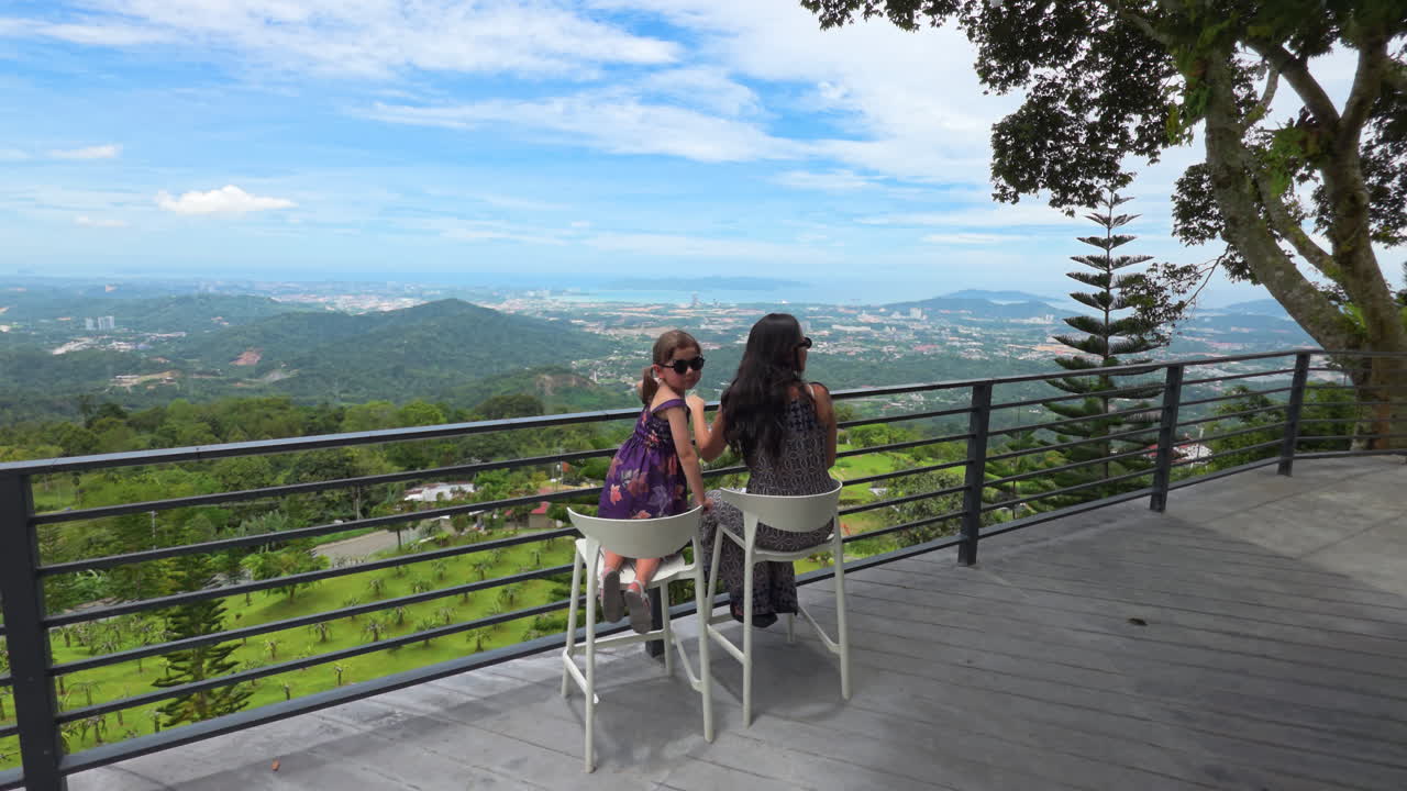 Mom And Daughter Sit On The Veranda Of The Hillside Cafe In Kokol Hill Near Kota Kinabalu, Sabah, Malaysia. POV Shot