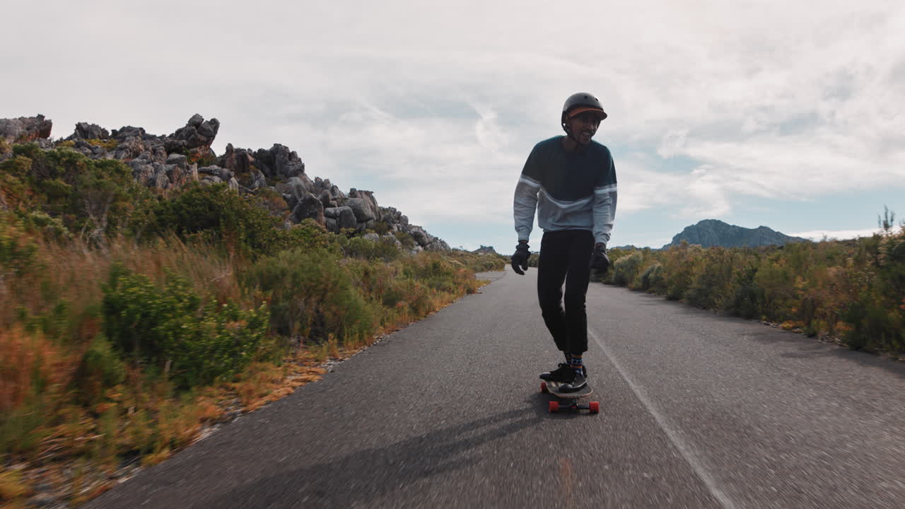 giovane afroamericano che cavalca un longboard pattinando velocemente godendosi la discesa su una strada di campagna facendo trucchi usando lo skateboard in slow motion