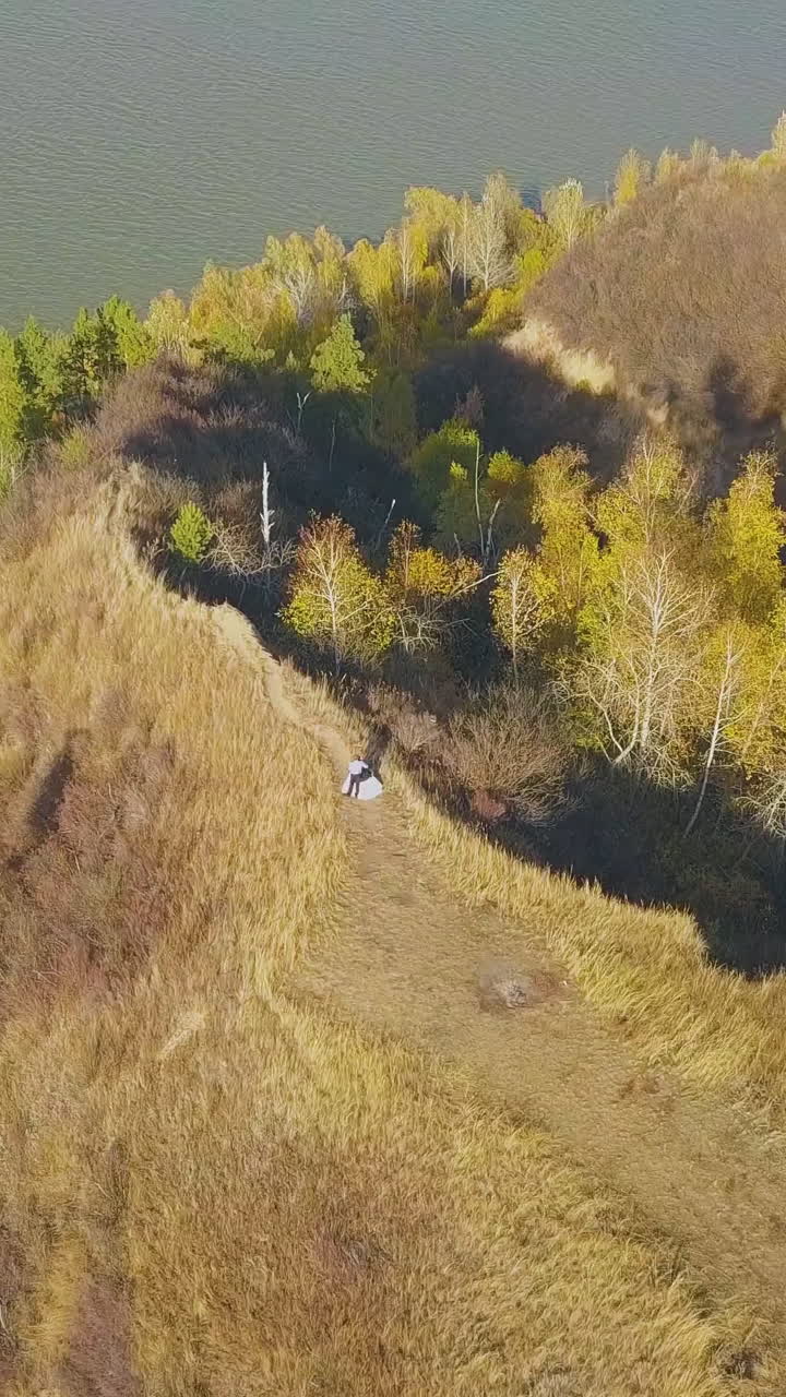 just married couple stands on steep hill with dry grass near calm river on autumn day bird eye view
