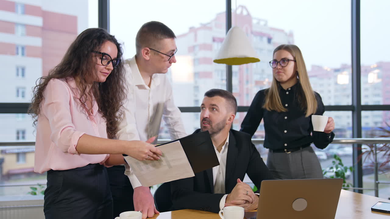 Long-haired brunet woman holding documents in her hands showing them to colleagues. Office team approve what they hear and nod heads.
