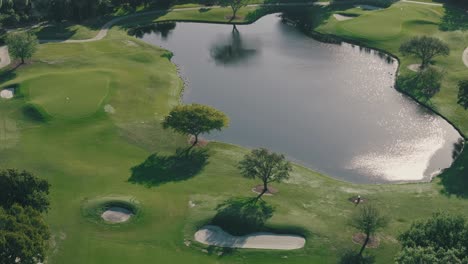 A-pond,-sand-traps,-and-trees-casting-long-shadows-sit-on-a-green-golf-course-in-Florida-on-a-sunny-afternoon