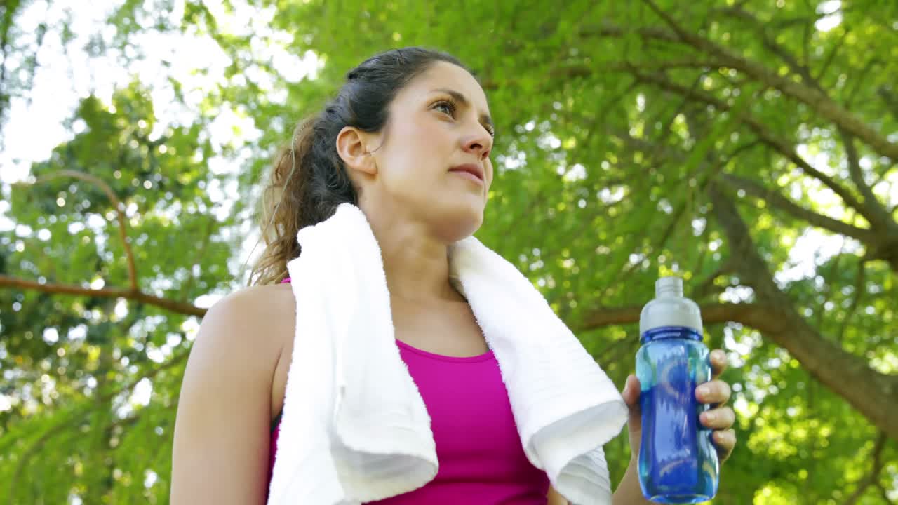 mujer limpiando la frente y bebiendo agua después de hacer ejercicio en el parque
