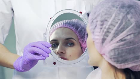 doctor holds the mirror and the patient looks at her lips and smiles in a beauty salon. the process of lips enhancement