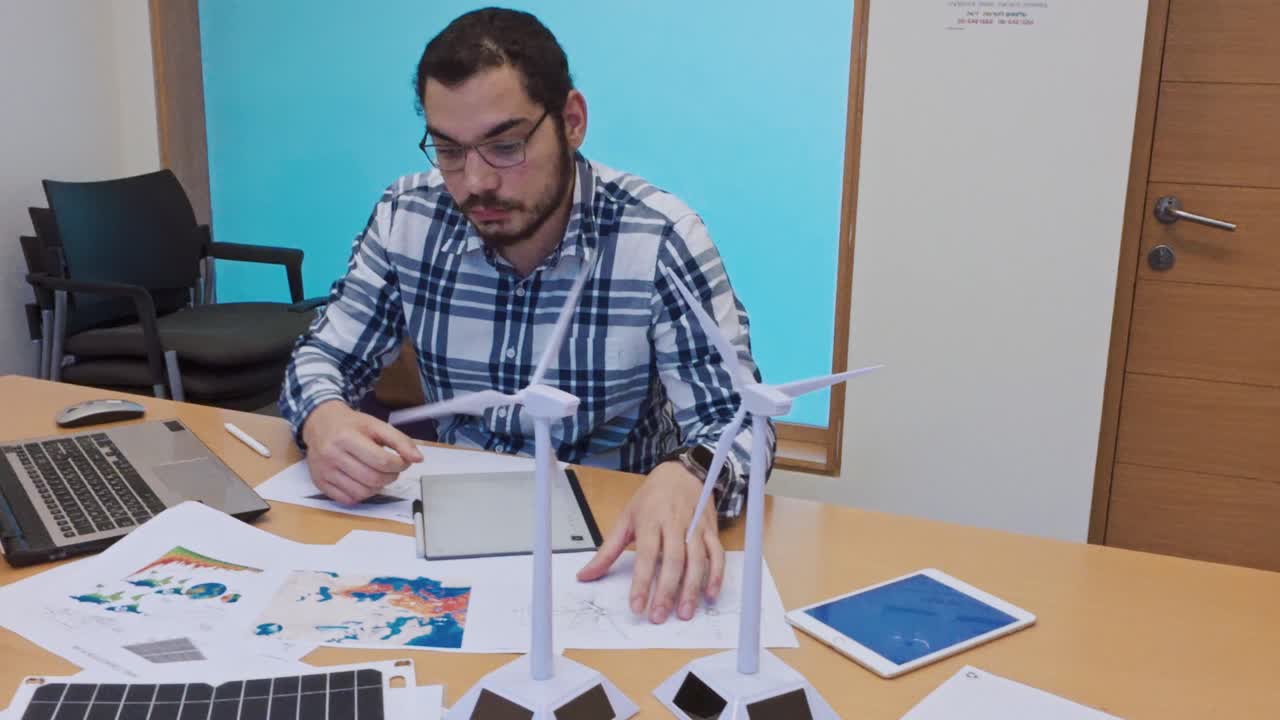 Man working on sustainable energy project with wind turbines and solar panel models