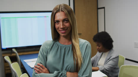 Portrait-of-caucasian-businesswoman-smiling-in-office,-with-colleague-working-in-background