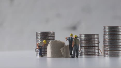 miniature workers working and piles of coins.